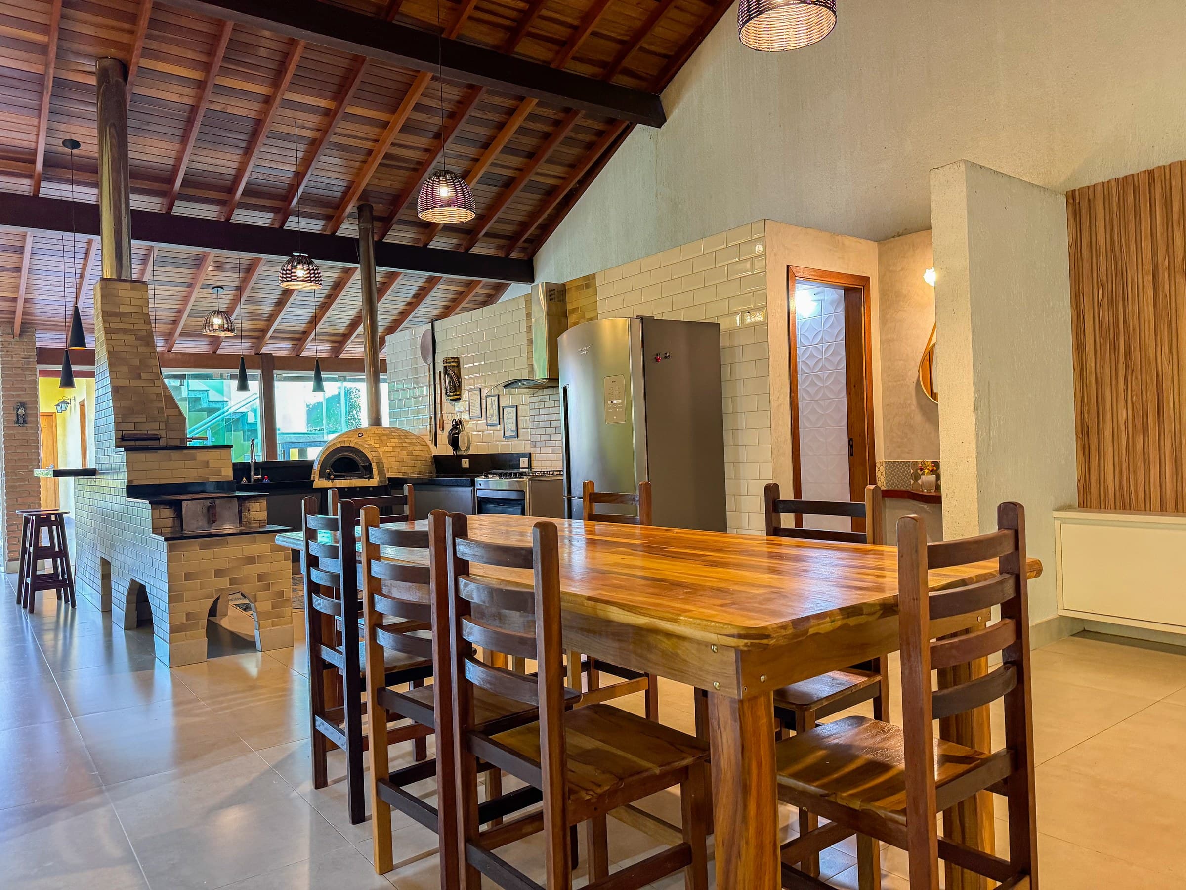 Ambiente integrado com mesa de jantar em madeira maciça, cozinha gourmet completa e estrutura ideal para refeições, confraternizações e momentos especiais entre familiares e convidados.
