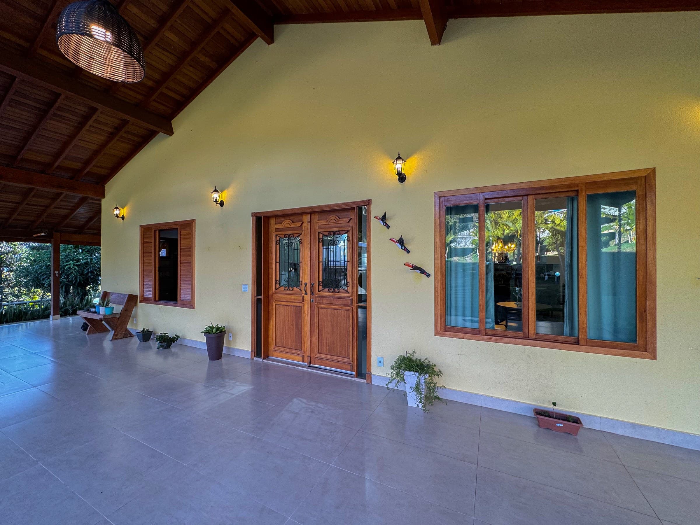 Ampla varanda coberta que recebe os convidados com elegância, oferecendo um ambiente acolhedor, integrado aos jardins e à arquitetura da Casa Principal.